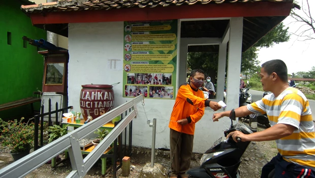 Petugas memeriksa suhu tubuh warga sebelum masuk ke kawasan Desa Mindaka di Kabupaten Tegal, Jawa Tengah, Sabtu, 13 Maret 2021. Mindaka menjadi salah satu desa percontohan pelaksanaan PPKM mikro.
