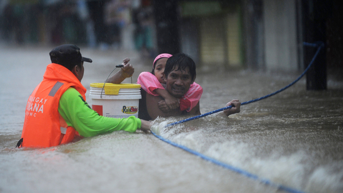 Seorang pria  dengan membawa anaknya berusaha melewati kawasan yang dilanda banjir di  Marikina, Manila, Filipina. FOTO:    AFP PHOTO / TED ALJIBE