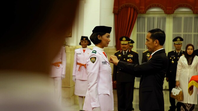 Presiden Joko Widodo (kanan) menyematkan pin tanda pengukuhan anggota Pasukan Pengibar Bendera (Paskibraka) tahun 2015 asal Lampung Della Elvira (kiri) di Istana Negara, Jakarta, Sabtu (15/8).