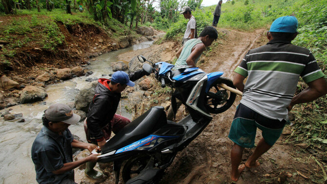 Sejumlah warga membantu pengendara motor menyeberangi sungai di Desa Kikia, Kabupaten Gorontalo Utara, Gorontalo, 27 Februari 2017.
