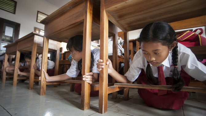 Sejumlah siswa berlindung di bawah bangku saat simulasi gempa bumi dan tsunami di SDN 2 Tanjung Benoa, Badung, Bali, 15 Agustus 2017. Simulasi yang melibatkan sekitar 400 siswa sekolah dasar, masyarakat, dan karyawan hotel tersebut merupakan proyek tanggap bencana oleh badan PBB, UNDP, di 18 negara di Asia Pasifik termasuk beberapa daerah di Indonesia.