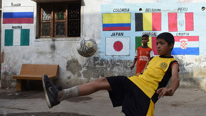 Dua anak Pakistan bermain bola di depan gambar bendera negara-negara peserta Piala Dunia 2018 di Lyari, Karachi, 13 Juni 2018.