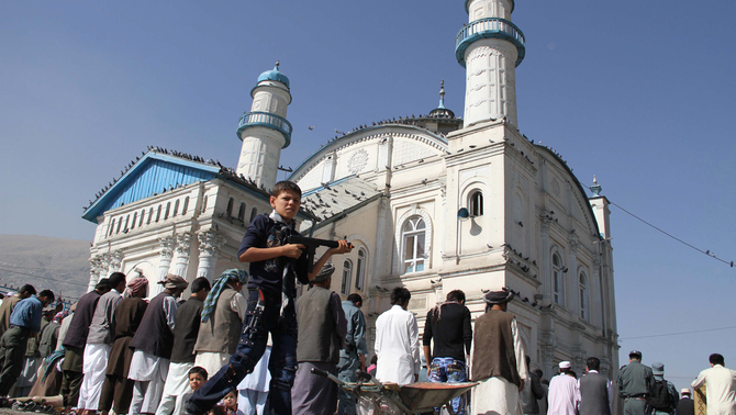 Seorang anak berjalan dengan memegang senjata mainan saat pelaksanaan salat Id di Kabul, Afghanistan. FOTO: EPA/S. SABAWOON