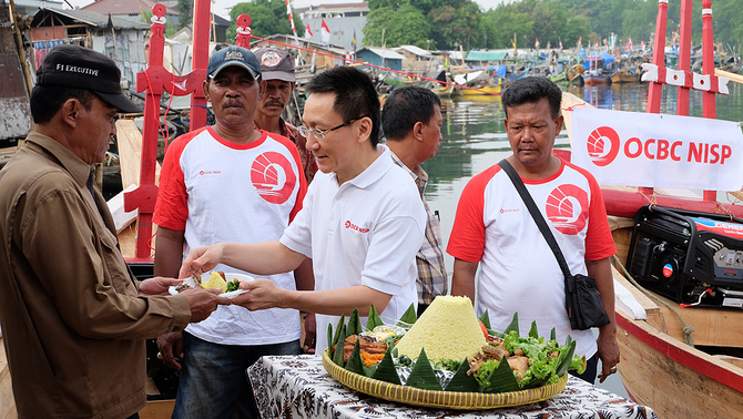 Direktur Bank OCBC NISP Rama P. Kusumaputra menyerahkan potongan tumpeng pertama kepadaKetua RW Kampung Nelayan Kali Adem H. Fayumi Naning sebagai simbolisasi rasa syukur acara pemberian perahu, 21 Agustus 2015.