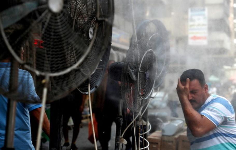 Seorang pria berdiri di dekat kipas angin menyemprotkan udara bercampur uap air yang dikerahkan oleh para donor untuk mendinginkan pejalan kaki di sepanjang jalan di ibu kota Irak, Baghdad pada Rabu 30 Juni 2021 di tengah gelombang panas yang parah. 