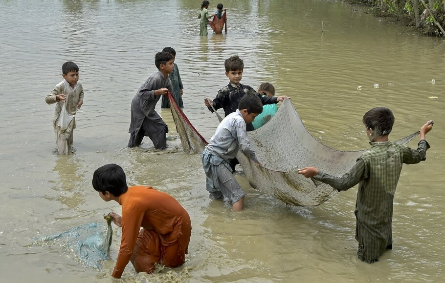 Anak-anak yang terdampak banjir menangkap ikan di sepanjang jalan yang banjir setelah hujan lebat di distrik Charsadda di provinsi Khyber Pakhtunkhwa pada 11 September 2022.
