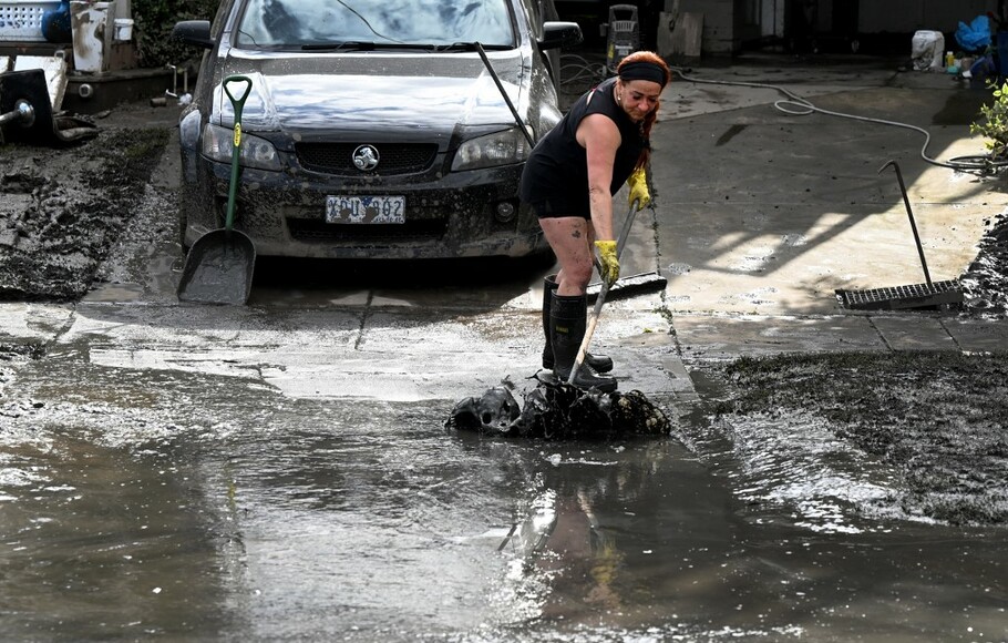 Seorang wanita membersihkan sisa lumpur yang dibawa banjir di pinggiran kota Melbourne, Maribyrnong pada 15 Oktober 2022.