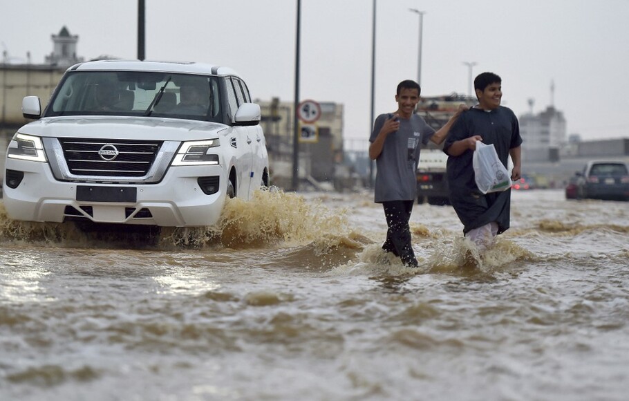 Warga berjalan di jalanan yang banjir akibat hujan lebat di kota pesisir Saudi Jeddah pada 24 November 2022 yang menunda penerbangan, memaksa penangguhan sekolah dan menutup jalan menuju Mekkah.