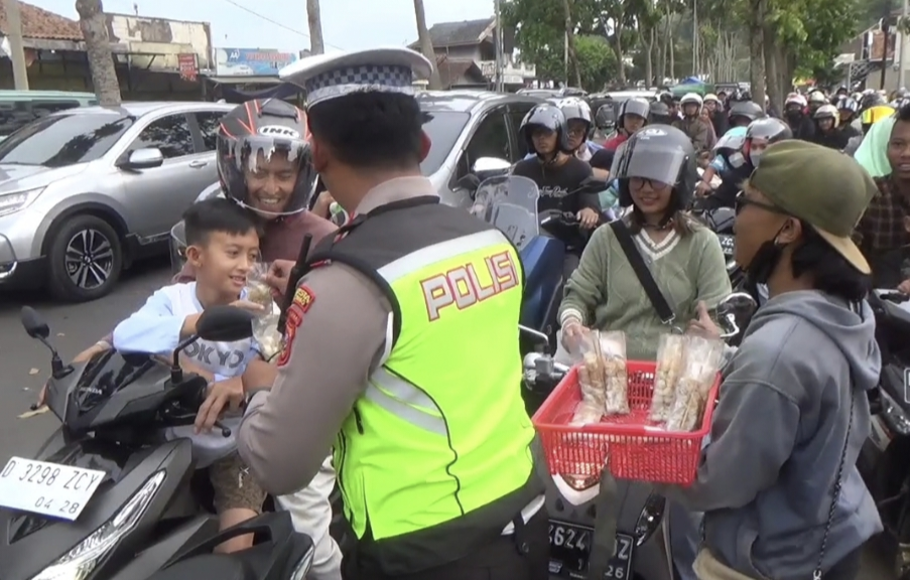 Petugas kepolisian membagikan cimol, jajanan khas Bandung pada wisatawan yang sedang terjebak macet dan menunggu sistem <em>one way</em> di jalur wisata Ciwidey, Selasa, 25 April 2023.