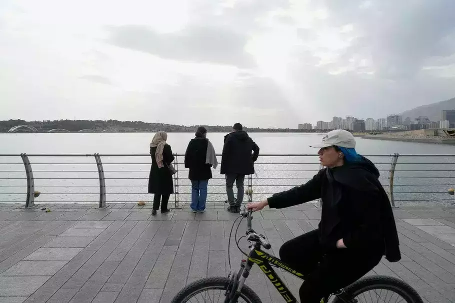 Orang-orang memandang danau buatan saat seorang wanita lewat dengan sepedanya selama liburan Tahun Baru Iran di Teheran barat, Iran, Minggu, 22 Maret 2026. - (AP/Vahid Salemi)