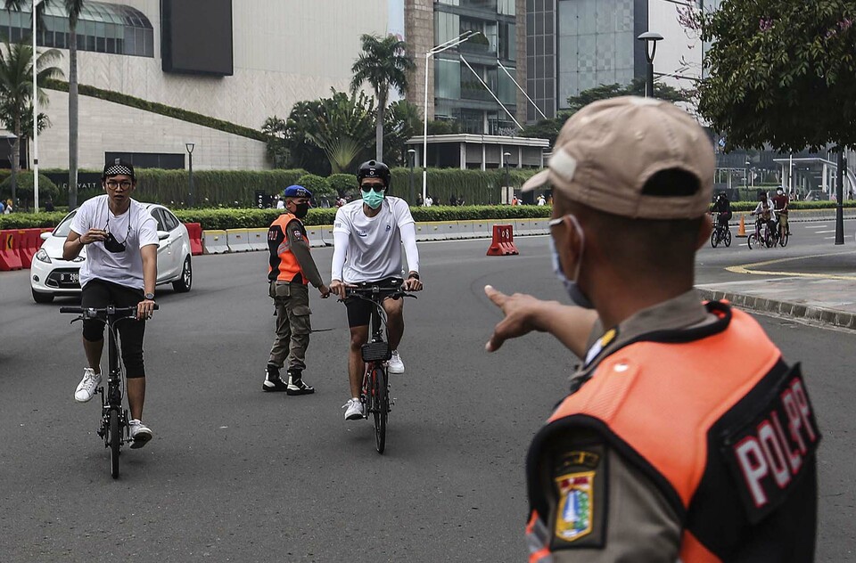 Petugas Satpol PP memberikan peringatan kepada warga yang berolahraga dengan bersepeda tidak memakai masker dengan benar di kawasan Bunderan HI, Jakarta Pusat, Minggu, 17 Januari 2021.