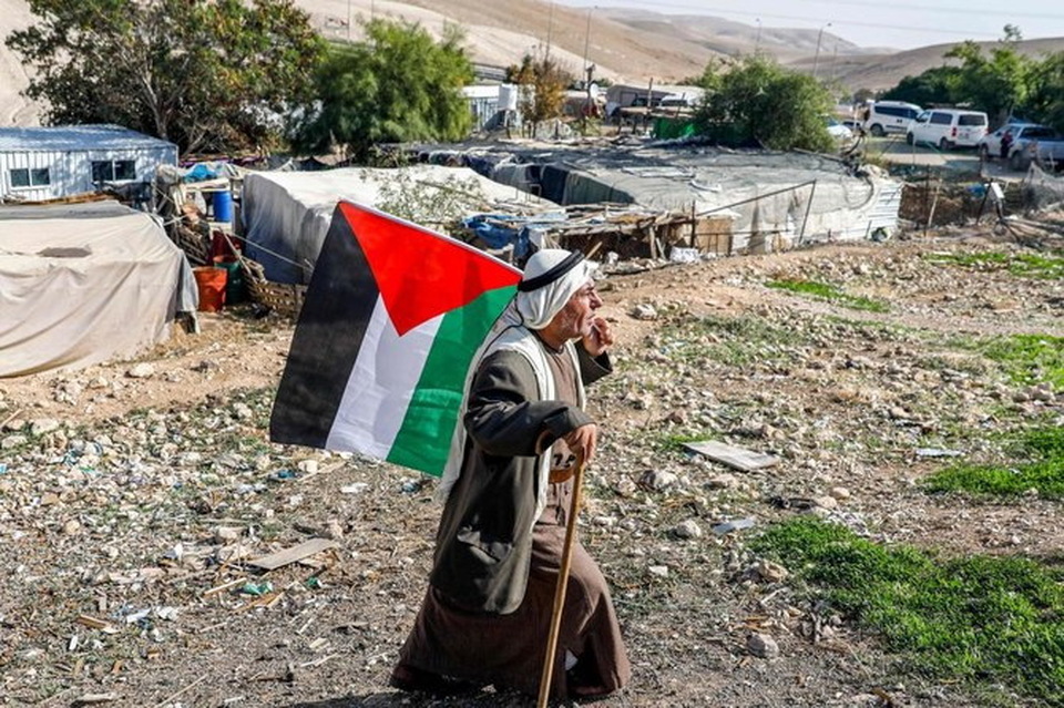 Seorang pria berjalan dengan bendera Palestina di desa Khan Al-Ahmar di Tepi Barat yang diduduki Israel pada 29 November 2020. 