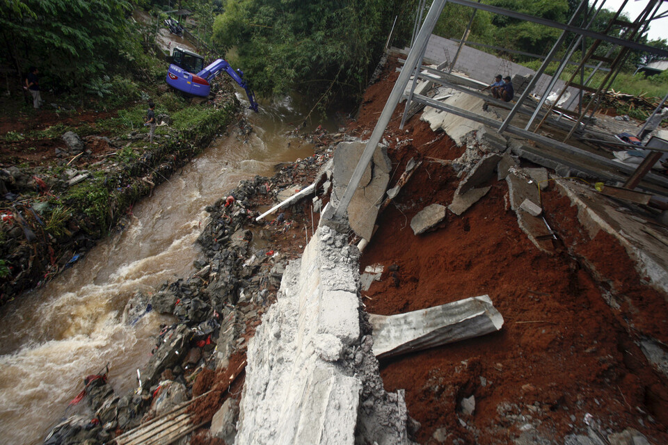 Sebuah alat berat mengangkut material longsor yang jatuh ke aliran Sungai Pesanggrahan, Raga Jaya, Bojonggede, Kabupaten Bogor, Jawa Barat, Selasa, 9 Februari 2021. Longor disebabkan luapan sungai yang menggerus turap di bantaran sungai. 