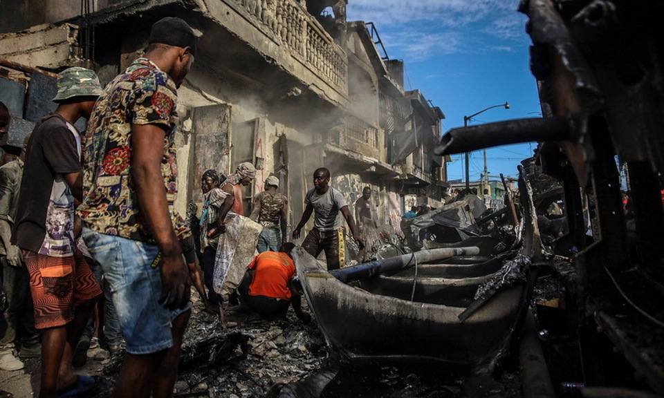 Para pria mengambil potongan aluminium di lokasi ledakan truk tangki di Cap-Haitien, Haiti akibat kekerasan geng bersenjata pada 14 Desember 2021. 