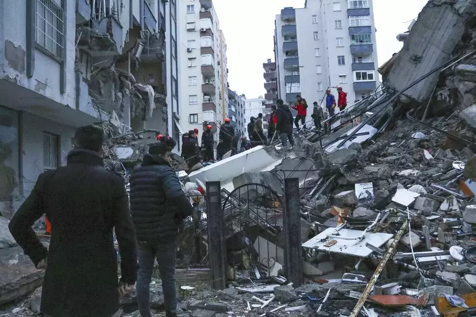 Warga sekitar dan tim penyelamat berusaha menjangkau warga yang terperangkap di dalam bangunan yang runtuh di Adana, Turki, Senin, 6 Februari 2023.