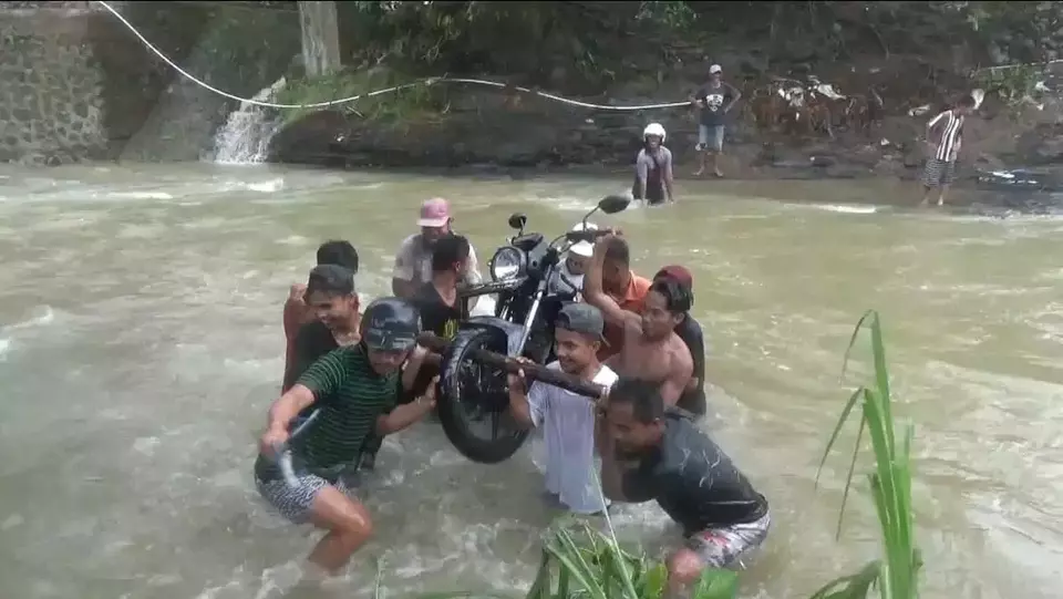 Warga bergotong-royong mengangkat motor untuk menyeberangi sungai di Desa Kunyi, Kecamatan Anreapi, Kabupaten Polewali Mandar, Sulawesi Barat, Kamis 23 Maret 2023.