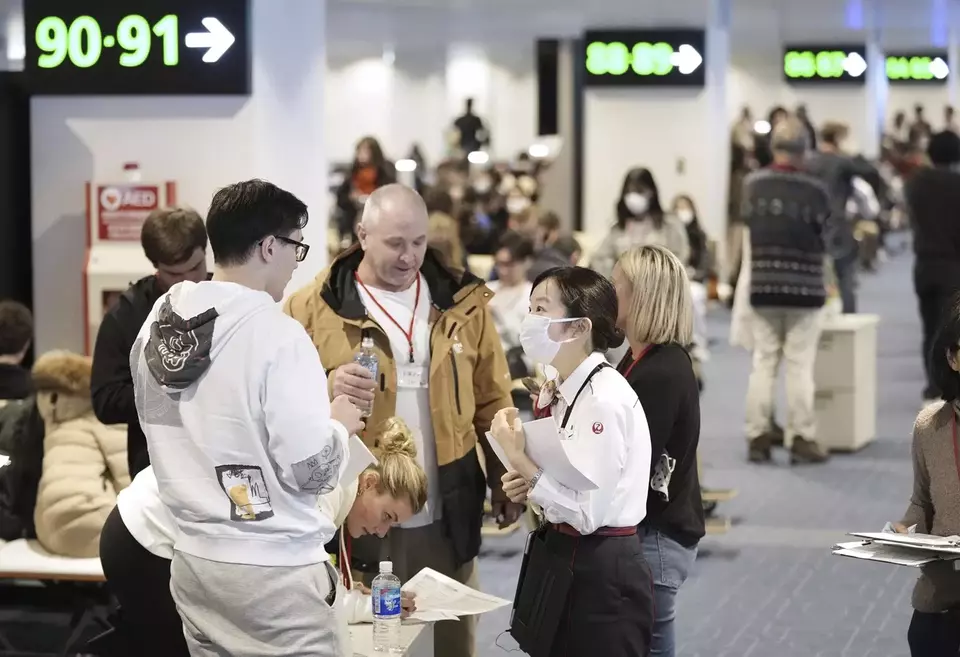 Petugas maskapai Japan Airlines berbicara dengan penumpang pesawat terbakar yang dievakuasi di bandara Haneda, Tokyo, Jepang, pada Selasa, 2 Januari 2024. 
