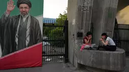 Warga Teheran berada di samping potret Pemimpin Tertinggi Iran Ayatollah Mojtaba Khamenei di gerbang utama Universitas Teheran, Iran, Selasa (12/5/2026). (Foto: AP/ Vahid Salemi)