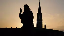 Seorang wanita memeriksa ponselnya sambil berjalan melewati Lapangan Merah saat matahari terbenam di Moskow, Rusia pada 31 Maret 2026. (Foto: AP/ Pavel Bednyakov)
