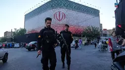 Para polisi berjalan di depan spanduk besar yang menampilkan bendera Iran di Lapangan Revolusi Islam di Teheran, Iran, Minggu (14/6/2026). (Foto: AP/ Vahid Salemi)