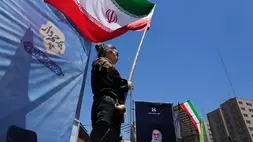 Seorang wanita mengibarkan bendera Iran selama kampanye pro-pemerintah sementara potret mendiang Pemimpin Tertinggi Ayatollah Ali Khamenei, yang tewas dalam serangan AS dan Israel pada 28 Februari, dipajang di sebelah kanan, di pusat kota Teheran, Iran, Senin (15/6/2026). (Foto: AP/ Vahid Salemi)
