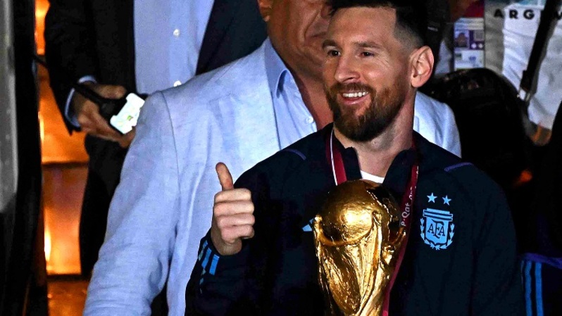 Kapten dan penyerang Argentina Lionel Messi (tengah) memegang Trofi Piala Dunia FIFA setibanya di Bandara Internasional Ezeiza setelah memenangkan turnamen Piala Dunia Qatar 2022, di Ezeiza, Provinsi Buenos Aires, Argentina pada 20 Desember 2022. (Foto: Luis ROBAYO / AFP)