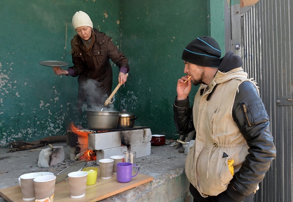 Seorang wanita memasak makanan di atas api terbuka karena kurangnya gas dan listrik di tengah serangan Rusia yang sedang berlangsung ke Ukraina, di kota timur laut Kharkiv pada 20 Maret 2022. (FOTO: Sergey BOBOK / AFP)