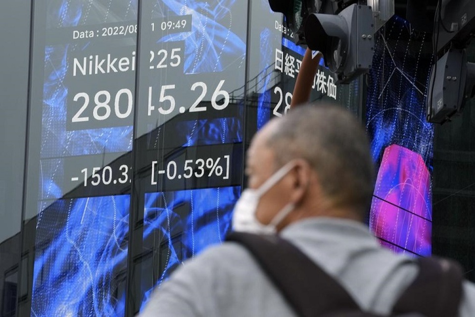 Seseorang yang mengenakan masker pelindung berdiri di depan papan stok elektronik yang menunjukkan indeks Nikkei 225 pada 31 Agustus 2022 di Tokyo, Jepang. (FOTO: AP/Eugene Hoshiko)