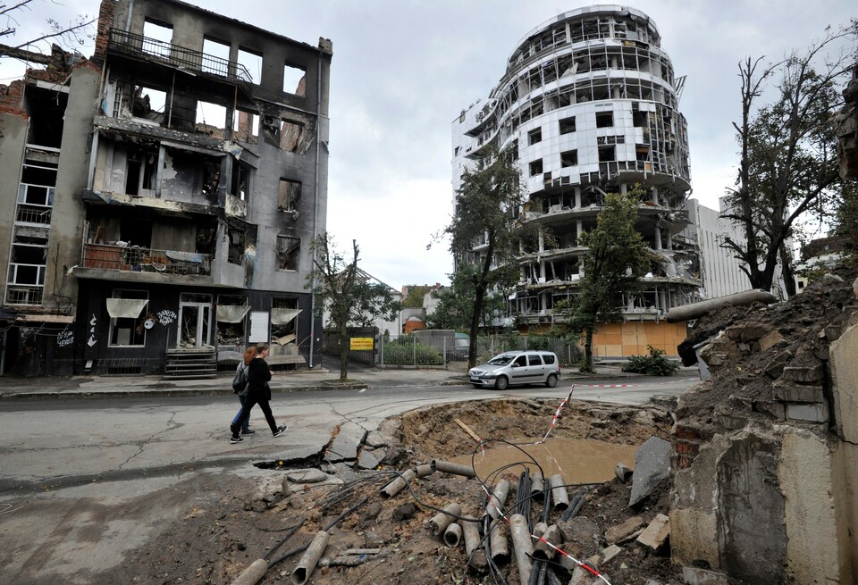 Warga berjalan melewati gedung-gedung yang hancur setelah aksi penembakan di pusat Kharkiv, beberapa waktu lalu, dalam invasi Rusia ke Ukraina. ( Foto: Sergei Chuzavkov/AFP)