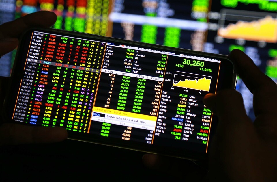 Pengguna telepon seluler melihat pergerakan harga saham. (BeritaSatu Photo/Mohammad Defrizal)