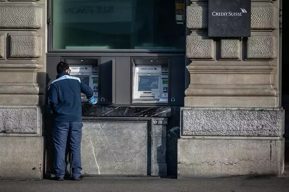 Seorang anggota staf membersihkan mesin ATM di kantor pusat bank Credit Suisse di Zurich, Swiss pada 20 Maret 2023. (Foto: Fabrice COFFRINI / AFP)