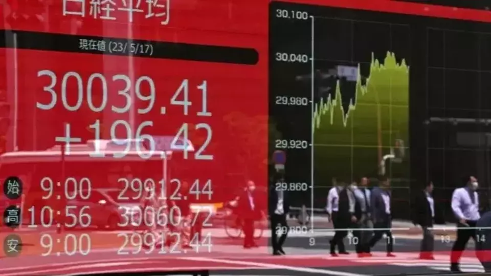 Bayangan orang-orang dalam papan kutipan elektronik yang menampilkan Nikkei Stock Average 225 edisi (atas) saat melintasi jalan di Tokyo, Jepang pada 17 Mei 2023. (Foto: Kazuhiro NOGI / AFP)