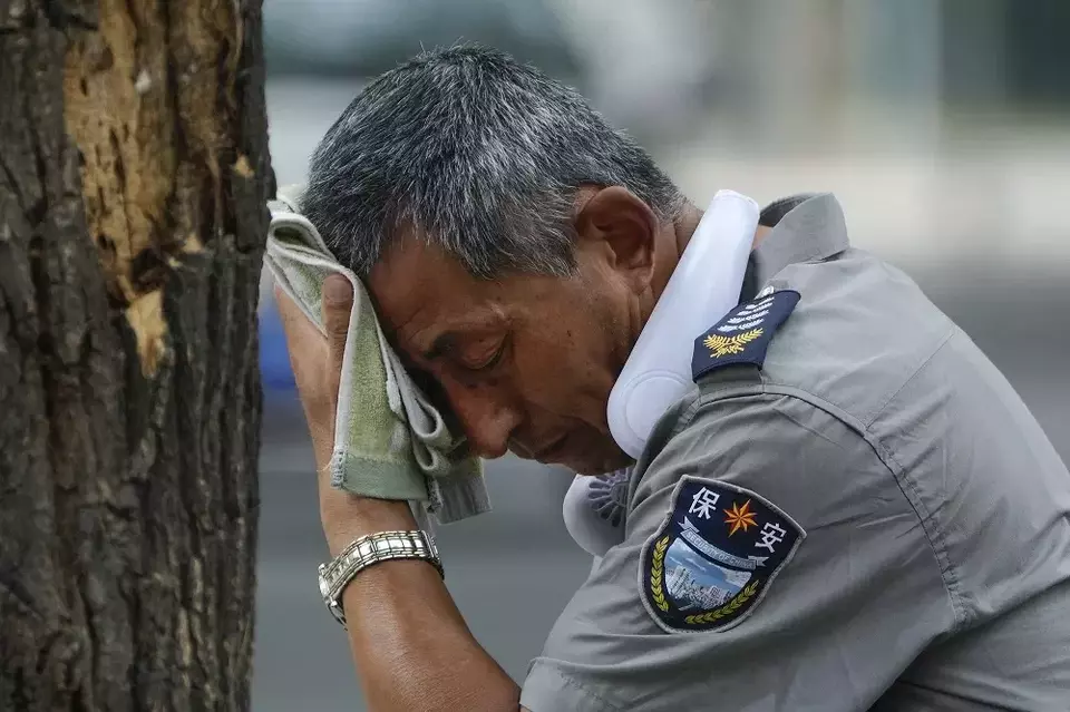 Seorang anggota satpam menyeka keringat sambil di lehernya tergantung kipas listrik mini di hari yang panas menyengat di Beijing, Tiongkok pada 3 Juli 2023. (Foto: Investor Daily/AP Photo/Andy Wong)