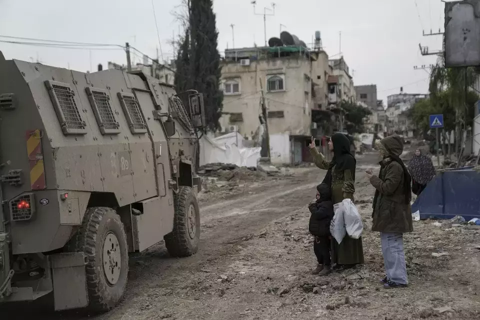 Seorang perempuan Palestina meengacungkan tanda V kepada tentara Israel yang lewat di depannya, dalam serangan drat di kamp pengungsi Tulkarem, tepi Barat, pada Rabu (17/01/2024). Retorika-retorika kasar Israel terhadap warga Palestina di Gaza, seperti "memerangi binatang manusia", menjadi komponen kunci gugatan Afrika Selatan di Mahkamah Internasional dan bukti bahwa Israel berniat melakukan genosida. (AP Photo/Nasser Nasser)