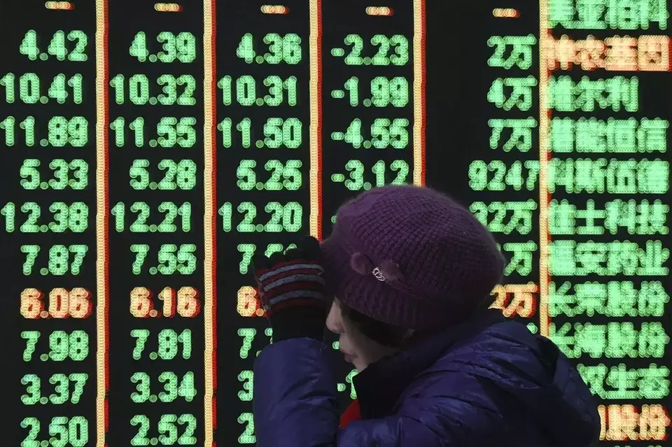 Seorang wanita melewati layar elektronik yang menampilkan harga saham di sebuah rumah pialang di Hangzhou, Provinsi Zhejiang, China timur pada 5 Februari 2024. (Foto: Chinatopix via AP, File)