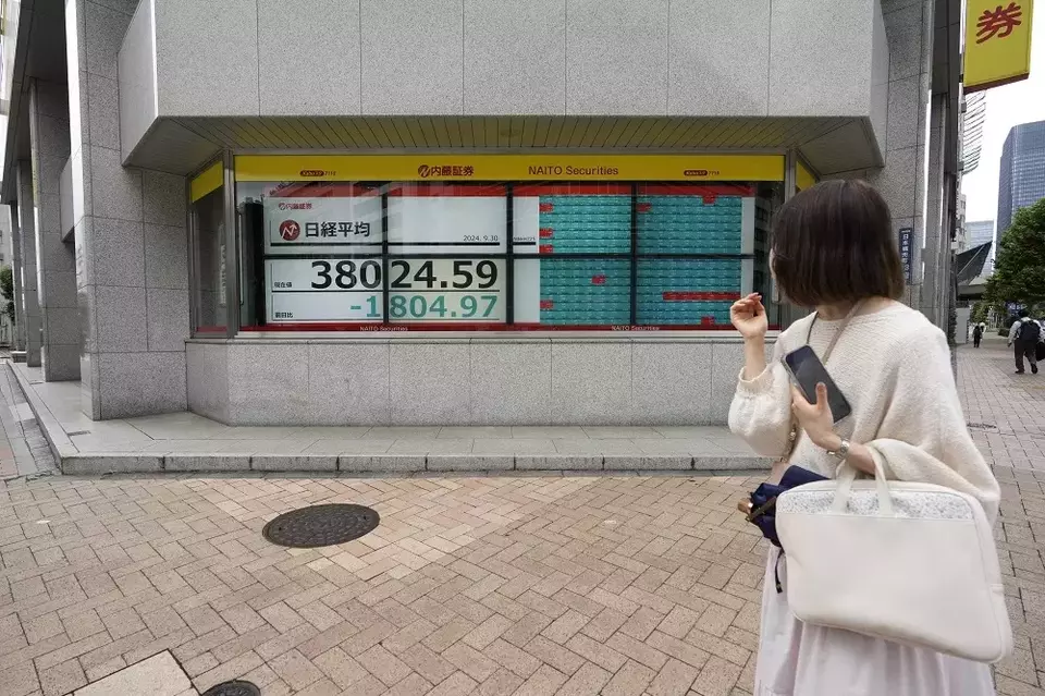 Seorang wanita melihat monitor yang menunjukkan indeks Nikkei 225 Jepang di sebuah perusahaan sekuritas saat dia menunggu di persimpangan lalu lintas di Tokyo, Jepang pada Senin (30/9/2024). (Foto: AP/Hiro Komae)