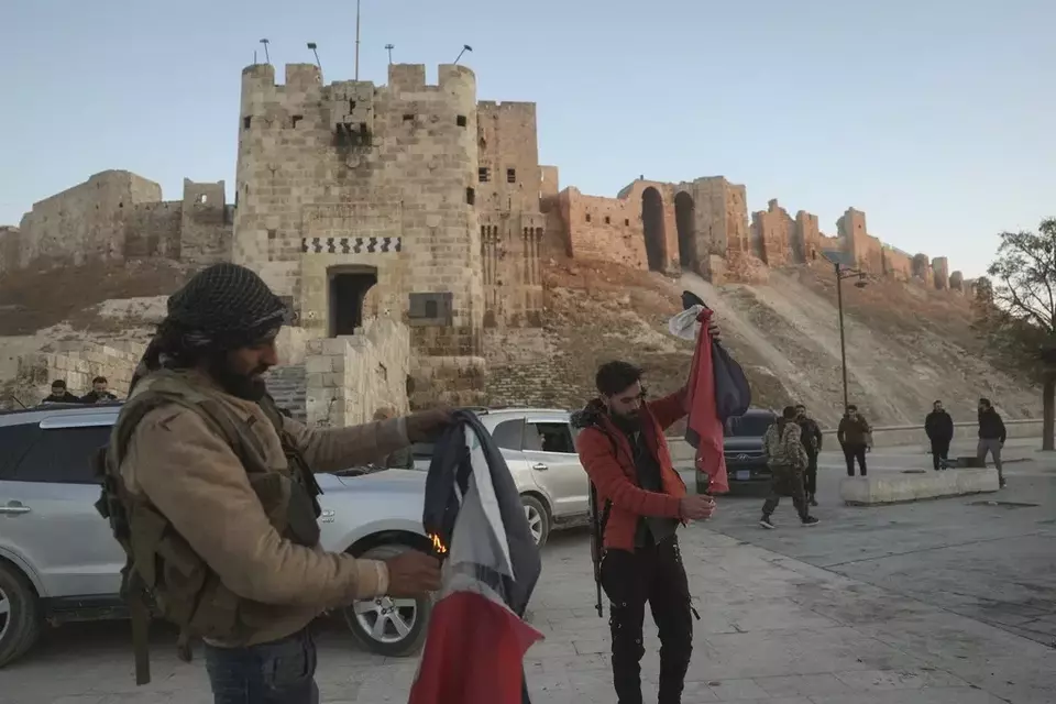 Pemberontak Suriah 
Pejuang oposisi Suriah membakar bendera pemerintah Suriah di depan kamera di samping kota tua Aleppo, Sabtu 30 November 2024. (Investor Daily/AP Photo/Ghaith Alsayed)
