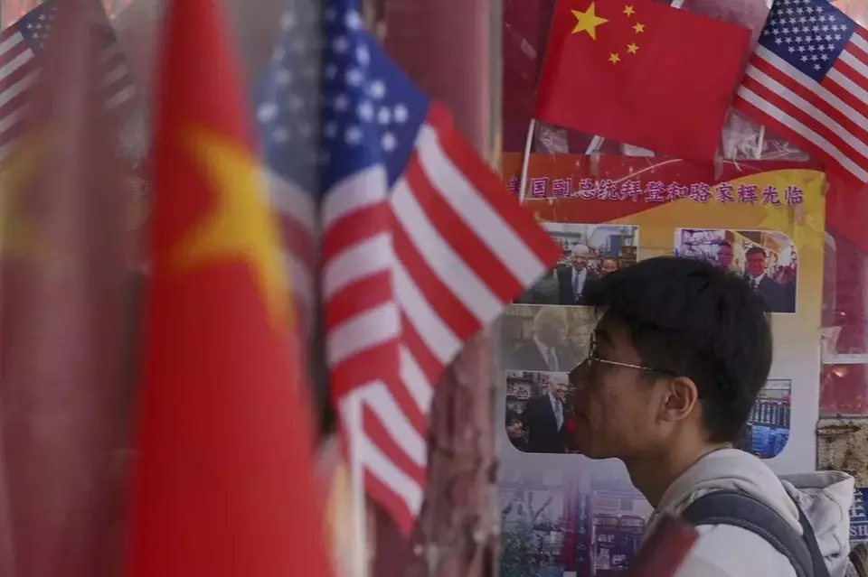 Seorang pria berjalan ke toko barang dagangan yang memajang bendera nasional China dan Amerika Serikat (AS) di Beijing, China pada Kamis (3/4/2025). (Foto: AP/ Andy Wong)