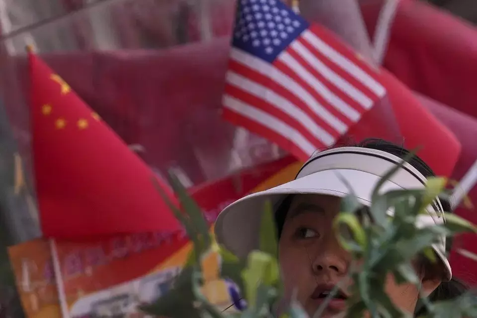 Seorang wanita berjalan melewati bendera nasional China dan Amerika Serikat (AS) yang dipajang di sebuah toko barang dagangan di Beijing, China pada Kamis (3/4/2025). (Foto: AP/ Andy Wong)