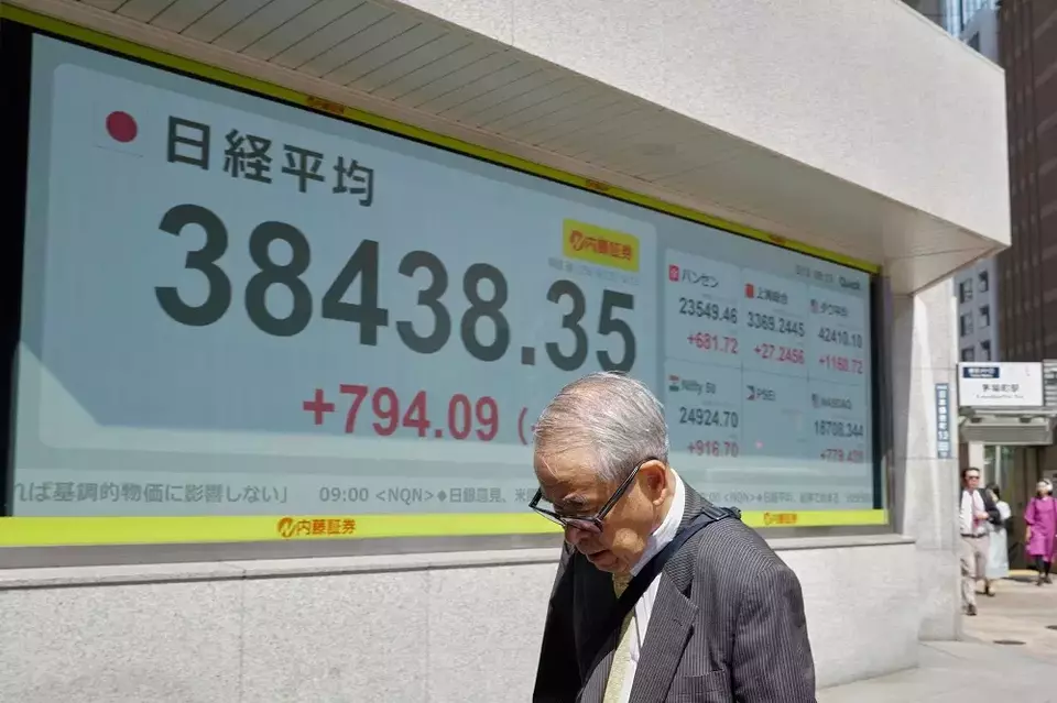 Seseorang berjalan di depan papan saham elektronik yang menunjukkan indeks Nikkei Jepang di sebuah perusahaan sekuritas pada Selasa (13/5/2025) di Tokyo, Jepang. (Foto: AP/ Eugene Hoshiko)