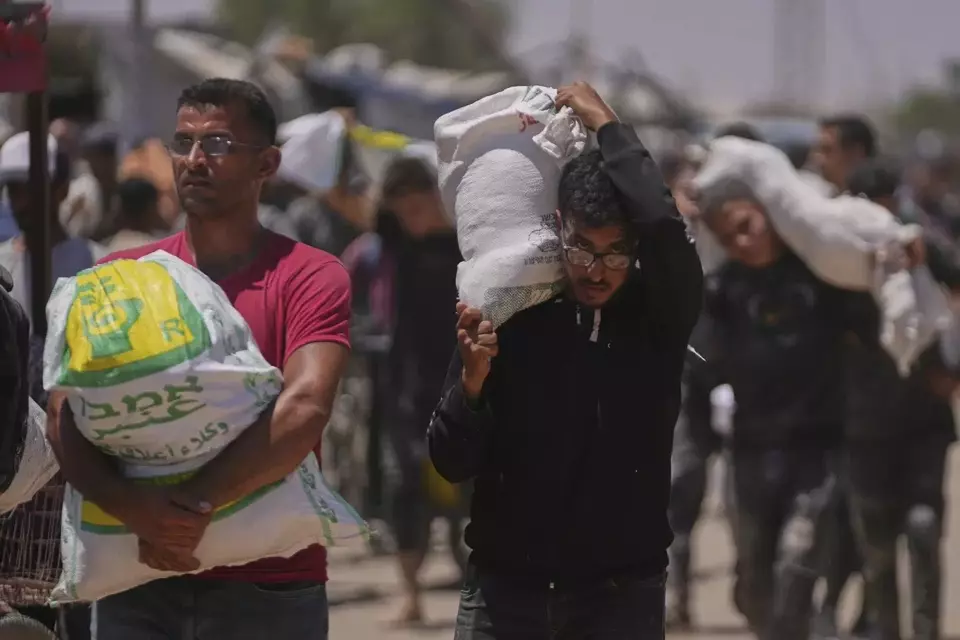Warga Palestina membawa karung berisi makanan dan paket bantuan kemanusiaan yang dikirim oleh Yayasan Kemanusiaan Gaza di Rafah, Jalur Gaza selatan, pada 25 Juni 2025. (AP Photo/Abdel Kareem Hana)