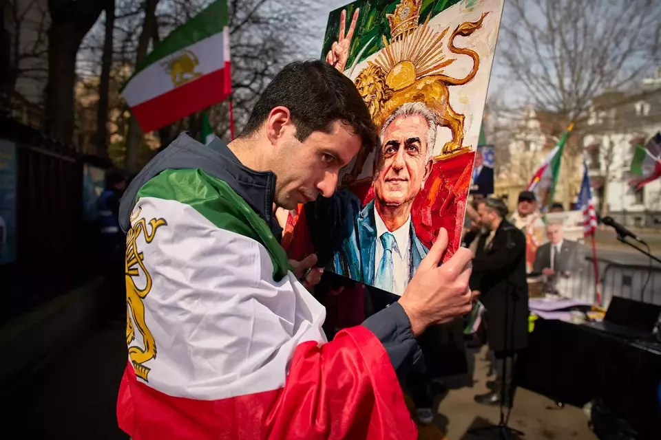 Seorang anggota komunitas Iran memegang poster putra mahkota Iran yang diasingkan, Reza Pahlavi, selama unjuk rasa di luar kedutaan Iran di Bucharest, Rumania, Kamis (5/3/2026). (Foto: AP/ Andreea Alexandru)