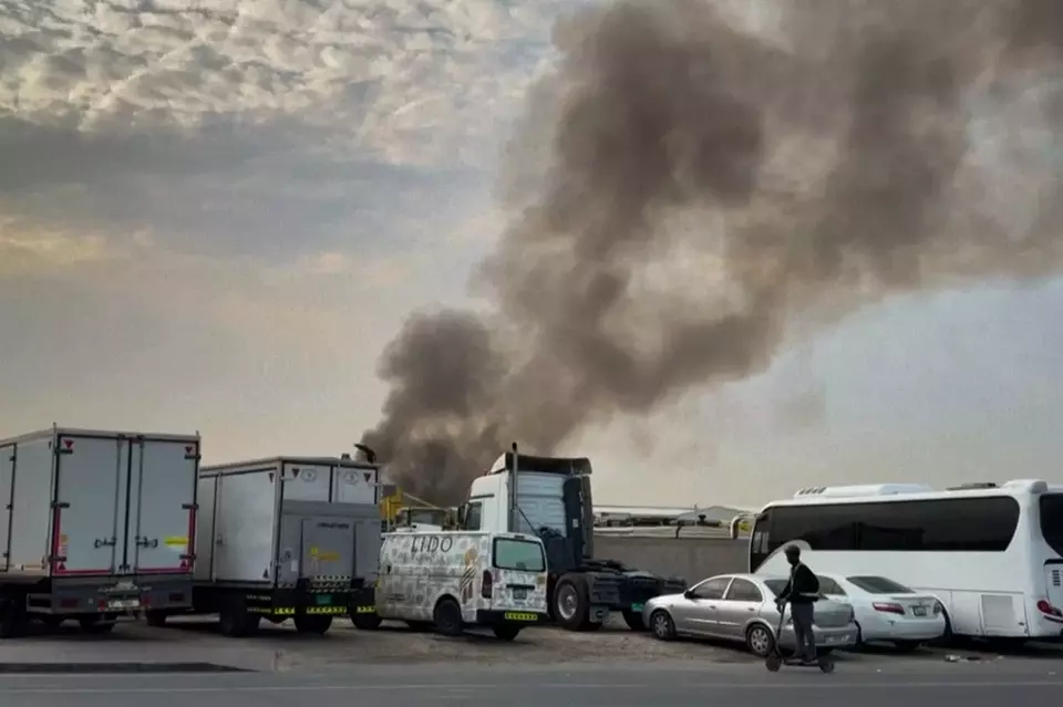 Gambar ini diambil dari sebuah video yang menunjukkan seorang pria berkendara melewati asap yang mengepul dari kebakaran yang, menurut pihak berwenang, disebabkan oleh pencegatan yang berhasil, di kawasan industri Al Quoz Dubai, Uni Emirat Arab, Sabtu (13/3/2026). (Foto: AP)