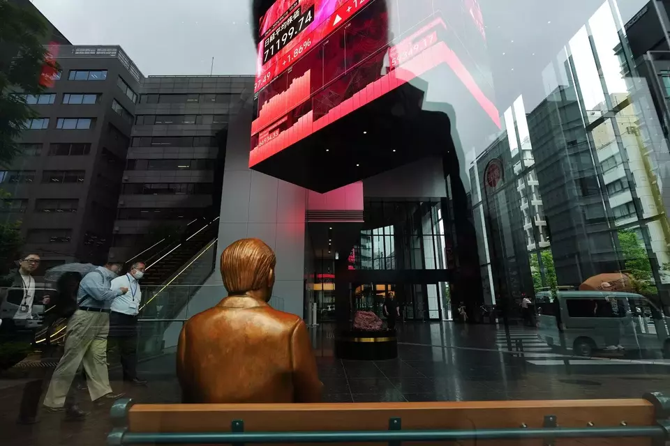 Sebuah patung diletakkan di bangku dekat monitor yang menampilkan indeks Nikkei 225 Jepang, yang tergantung di sebuah gedung perkantoran di Tokyo, Jepang pada Kamis (18/6/2026). (Foto: AP/ Hiro Komae)