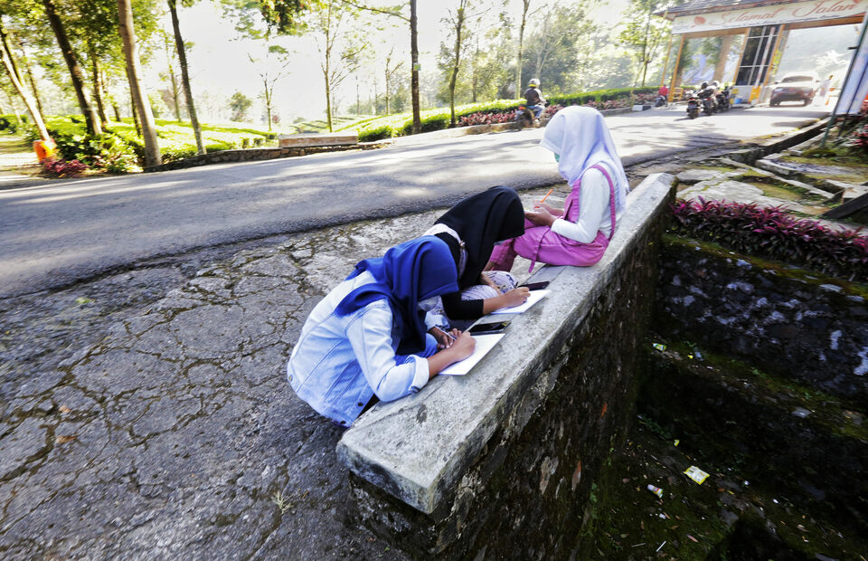 Junior high school students do their online homework at the roadside in search for better internet signal in Gunung Mas area, Bogor, West Java, on July 28, 2020. Most schools in Indonesia apply remote learning during the Covid-19 pandemic. (Beritasatu Photo/Ruht Semiono)