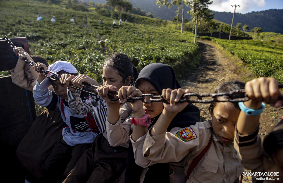 Students hold onto a chain as they hitchhike a truck to go to school at the Tugu Utara village in Bogor, West Java on June 2, 2022. (JG Photo/Yudha Baskoro)