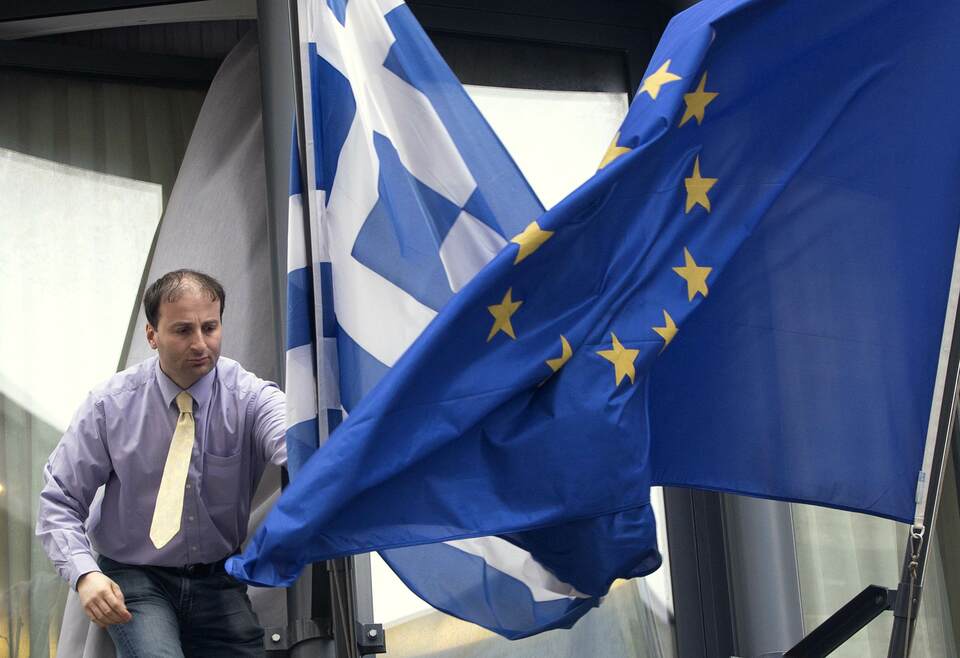 A man adjusts a Greek flag, left, and a European flag outside the Greek embassy in Brussels on Feb. 19, 2015. (Reuters Photo/Yves Herman)