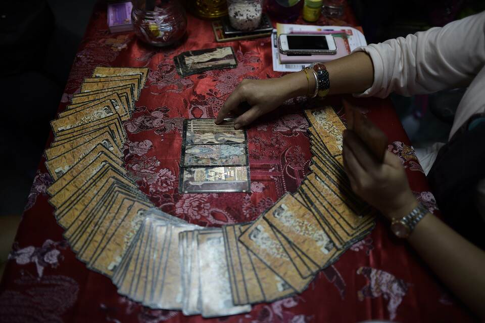 A fortune teller using tarot cards to predict the future of a woman (not pictured) at a Buddhist temple in Bangkok sheltering a shrine dedicated to the famous ghost 'Nak', a woman who Thais believe lived in Bangkok in the 19th century and died during childbirth while her husband was away fighting a war. (AFP Photo/Christophe Archambault)