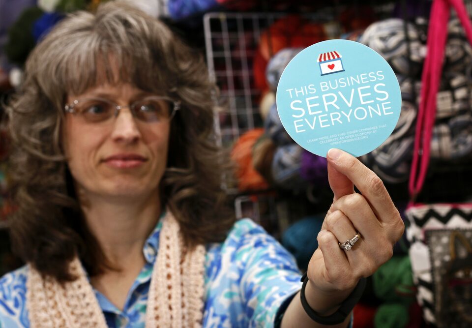 Elizabeth Ladd, owner of River Knits Fine Yarns, poses while holding up a ‘This businesses serves everyone’ sticker she plans to place outside her business in downtown Lafayette, Indiana on March 31, 2015. (Reuters Photo/Nate Chute)