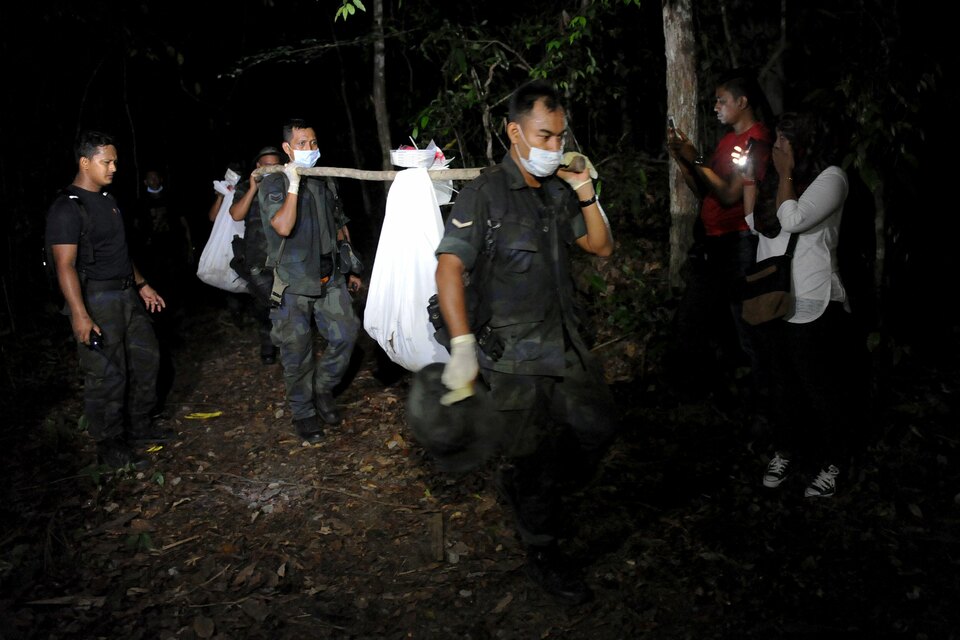 Policemen carry body bags with human remains recovered from the jungle close to the border with Thailand, at Wang Kelian in northern Malaysia on May 28. The mass graves were uncovered near people-smuggling camps in northern Malaysia. (Reuters Photo)